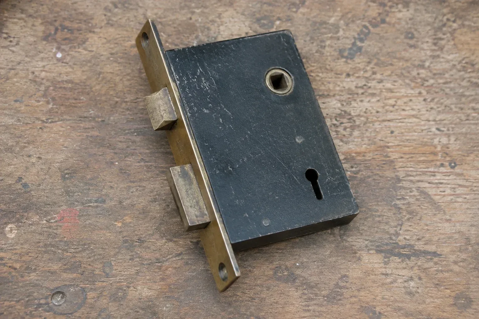 Closed mortise lock case with spindle opening, keyhole, latch and deadbolt on a wooden workbench. — Vintage Mortise Lock Service, Oshawa