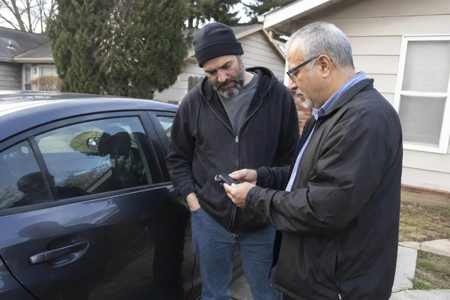 Two adults discussing a key fob beside a parked car. — Car Lockout Service, Oshawa